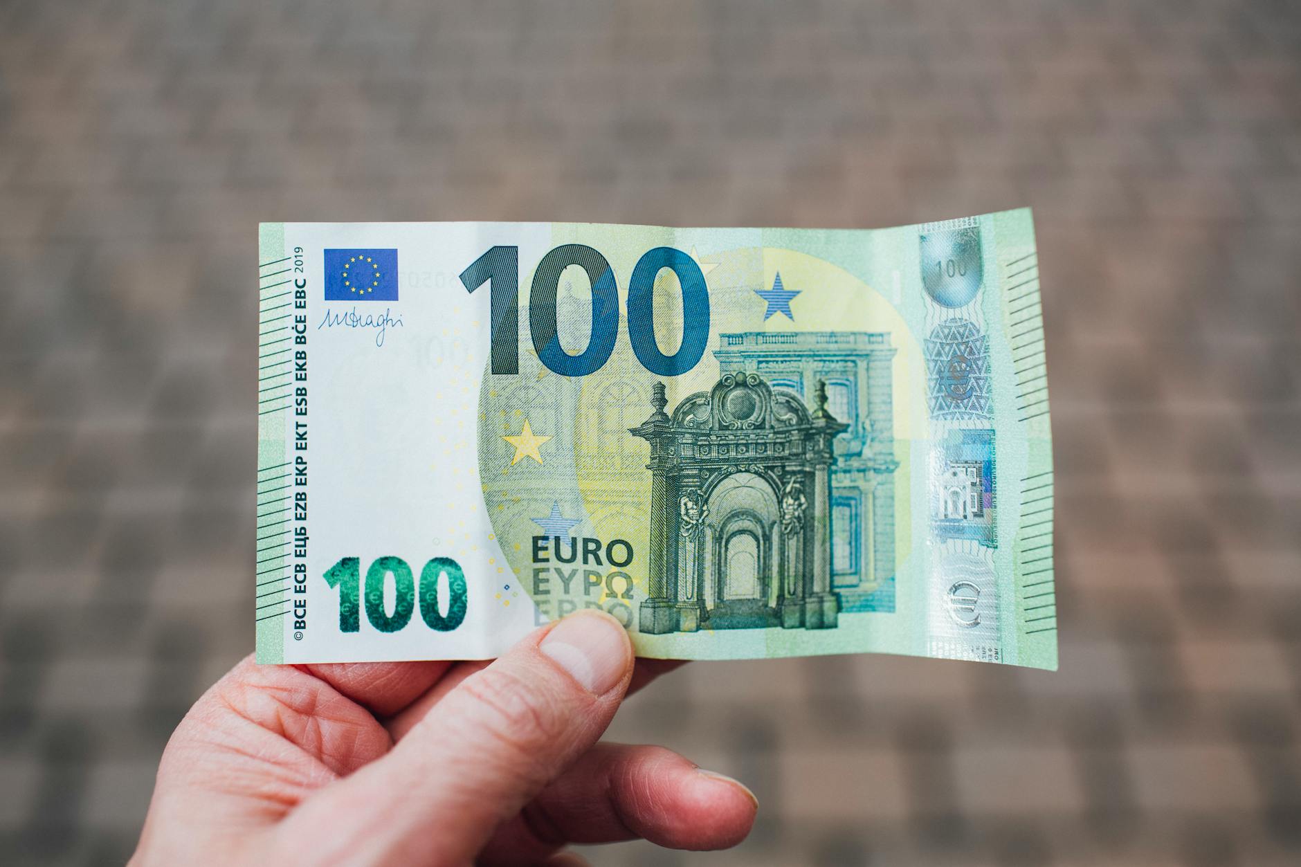 Dłoń trzymająca banknot 100 euro na rozmytym tle