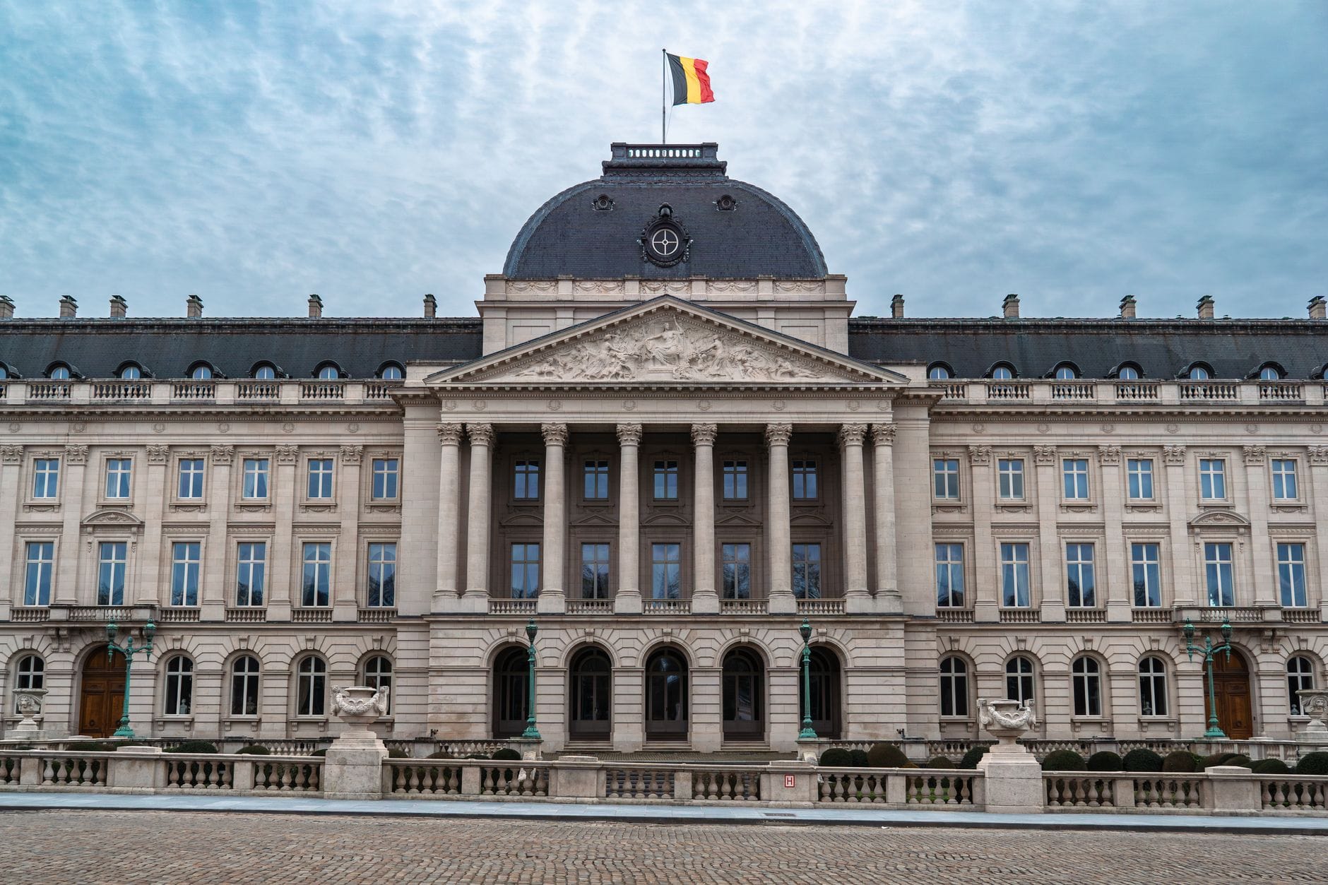 Polityka gospodarcza II RP między kryzysem a modernizacją czego uczy dziś Pałac Królewski w Brukseli z belgijską flagą pod pochmurnym niebem